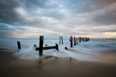 Waves wash through the poles on St Clair Beach, Dunedin, New Zealand.