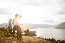 Mountain bike riders Casey Brown and Naomi Wilson overlook Lake Wakatipu on the Queenstown Bike Park at Skyline, Queenstown, New Zealand. 