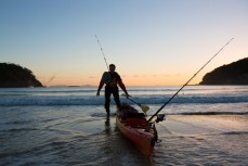Ryan drags his kayak down the beach at dawn for some fishing at Matapouri Bay, Northland, New Zealand.