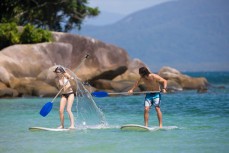 Robyn MacFarlane and Aaron Gallagher stand-up paddleboard around Fitzroy Island near Cairns in Tropical North Queensland, Queensland, Australia. 