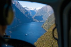 A boat cuts a path through calm waters of Milford Sound on a perfect day in Fiordland, New Zealand. 