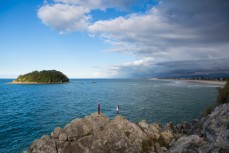 German tourists Inga and Yannik watch as a storm approaches the beaches and rocky outcrops of Mount Maunganui, New Zealand. 