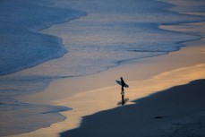 A surfer girl waits on the beach at dusk at Blackhead Beach, Dunedin, New Zealand. 