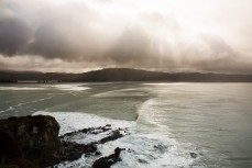 Rain clouds break up above a bay on the North Coast, Dunedin, New Zealand. 