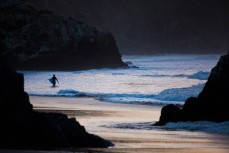 A surfer returns to the beach after a dusk session at Aramoana, Dunedin, New Zealand. 