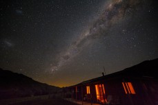 The Milky Way arcs over our a house illuminated by firelight at the remote Muzzle Station between the Seaward and Inland Kaikoura Ranges on the Clarence River near Kaikoura, New Zealand. 