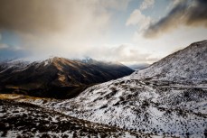 The Crown Range road cuts a trail through the tussockland as a spring storm sweeps through, Crown Range, New Zealand. 