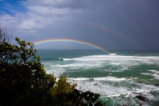 A rainbow illuminates the peak as a group of big wave surfers take on a storm swell in the Catlins, Otago, New Zealand. 