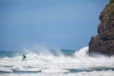 A surfer rides a frothy wave at a remote beach on Otago Peninsula, Dunedin, New Zealand. 