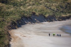 A group of surfers walk along a remote a beach on Otago Peninsula, Dunedin, New Zealand. 