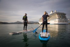 Craig Latta and Di Brenssell ride stand-up paddleboards on the Otago Harbour as a cruise ship Marina heads towards Port Chalmers, Dunedin, New Zealand. 