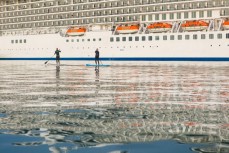 Craig Latta and Di Brenssell ride stand-up paddleboards on the Otago Harbour as a cruise ship Marina heads towards Port Chalmers, Dunedin, New Zealand. 