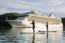 Craig Latta and Di Brenssell ride stand-up paddleboards on the Otago Harbour as a cruise ship Marina heads towards Port Chalmers, Dunedin, New Zealand. 