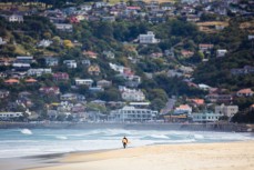 A lone surfer walks down the beach at St Clair, Dunedin, New Zealand. 