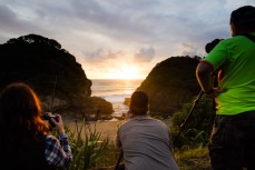 Members of the the Canon Collective Beach Culture Workshop watch the sun sink into the Tasman Sea at the beautiful Bethells Beach, Auckland, New Zealand. 