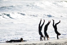 Surfer girls walk on their hands post-surf at St Kilda, Dunedin, New Zealand. 