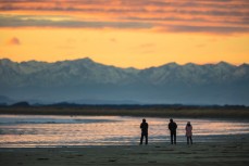 Tourists watch the sun set over the snow-capped peaks of Fiordland from Burt Munro's racetrack: Oreti Beach at Invercargill, New Zealand.