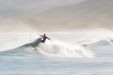 A surfer rides a wave in lazy spring waves at Blackhead Beach, Dunedin, New Zealand.