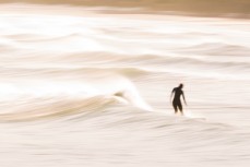 A surfer rides a wave in lazy spring waves at Blackhead Beach, Dunedin, New Zealand.
