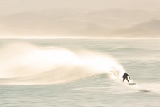 A surfer rides a wave in lazy spring waves at Blackhead Beach, Dunedin, New Zealand.