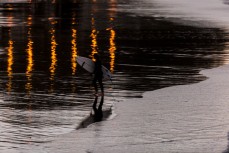 A surfer crosses in front of reflections at St Clair, Dunedin, New Zealand.