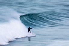 A surfer rides a clean, glassy waves at Blackhead, Dunedin, New Zealand.