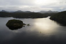 Heather stand-up paddleboards at dusk at Port Pegasus, Stewart Island, New Zealand.