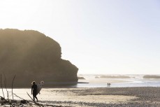 Surfers head to the water at Fox River, West Coast, New Zealand.