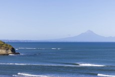 A wave breaks with Mt Egmont in the background, New Plymouth, Taranaki, New Zealand.