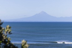 A wave breaks with Mt Egmont in the background, New Plymouth, Taranaki, New Zealand.