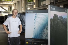 Surf photographer Oscar Hetherington with one of his finalist images in the 2024 New Zealand Geographic Photographer of the Year awards on display at Britomart in downtown Auckland, New Zealand.Photo: Derek Morrison