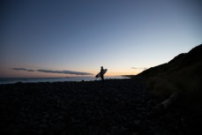 A surfer is silhouetted by sunset at Blackhead Beach, Dunedin, New Zealand.